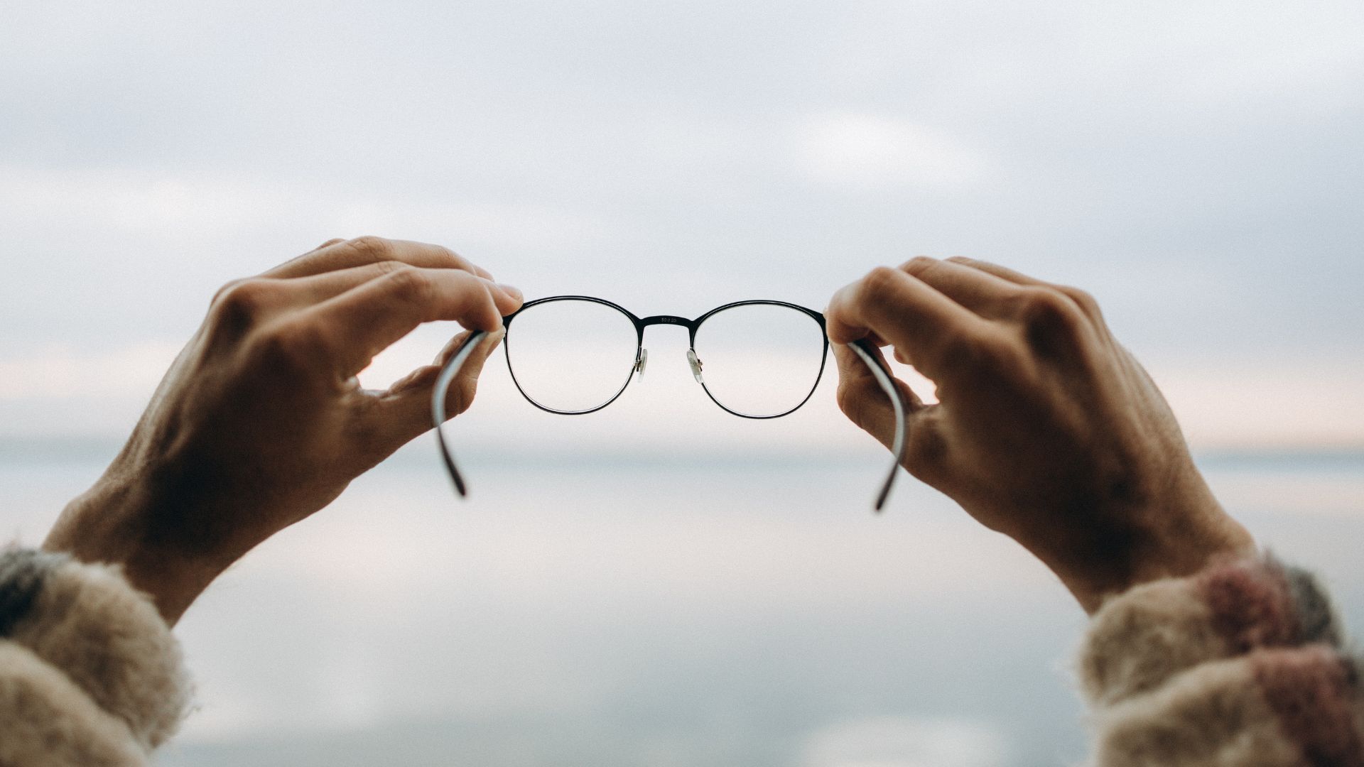 two hands holding a pair of eyeglasses