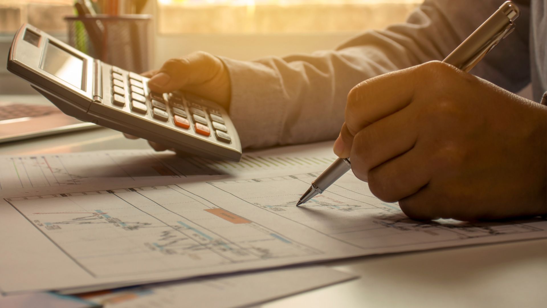 hands holding a pen in the left and a calculator in the right.